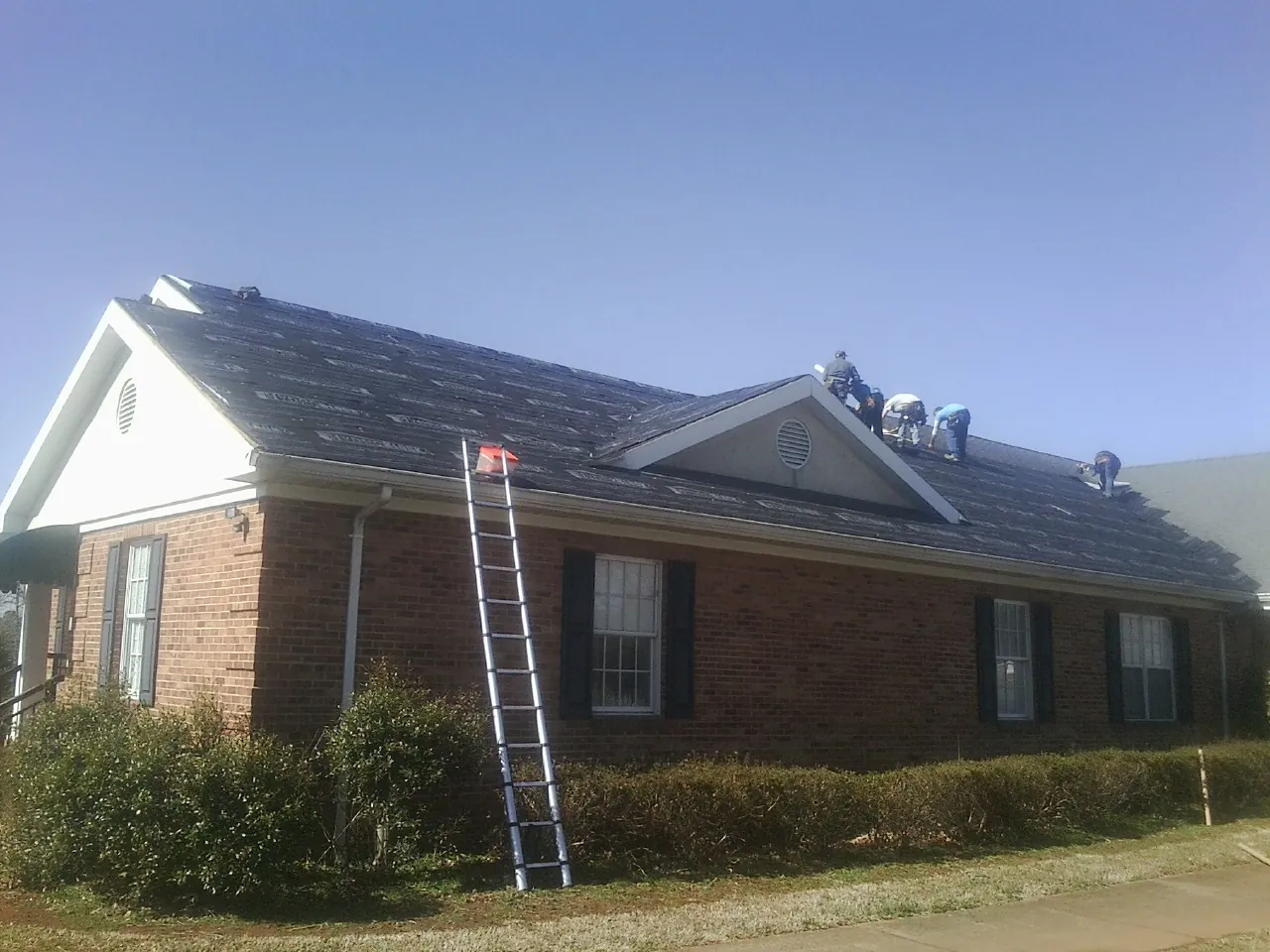 Crew tearing shingles off a brick ranch roof with a ladder set — Emergency Roof Repair work by our crew in Vacherie