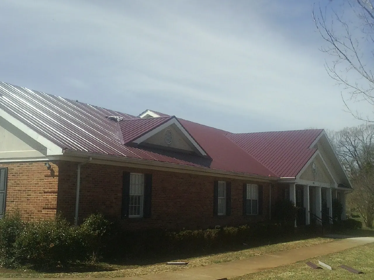 Red metal roof with gabled entries on a long brick building, from a Hail Damage Roof Repair job in Vacherie