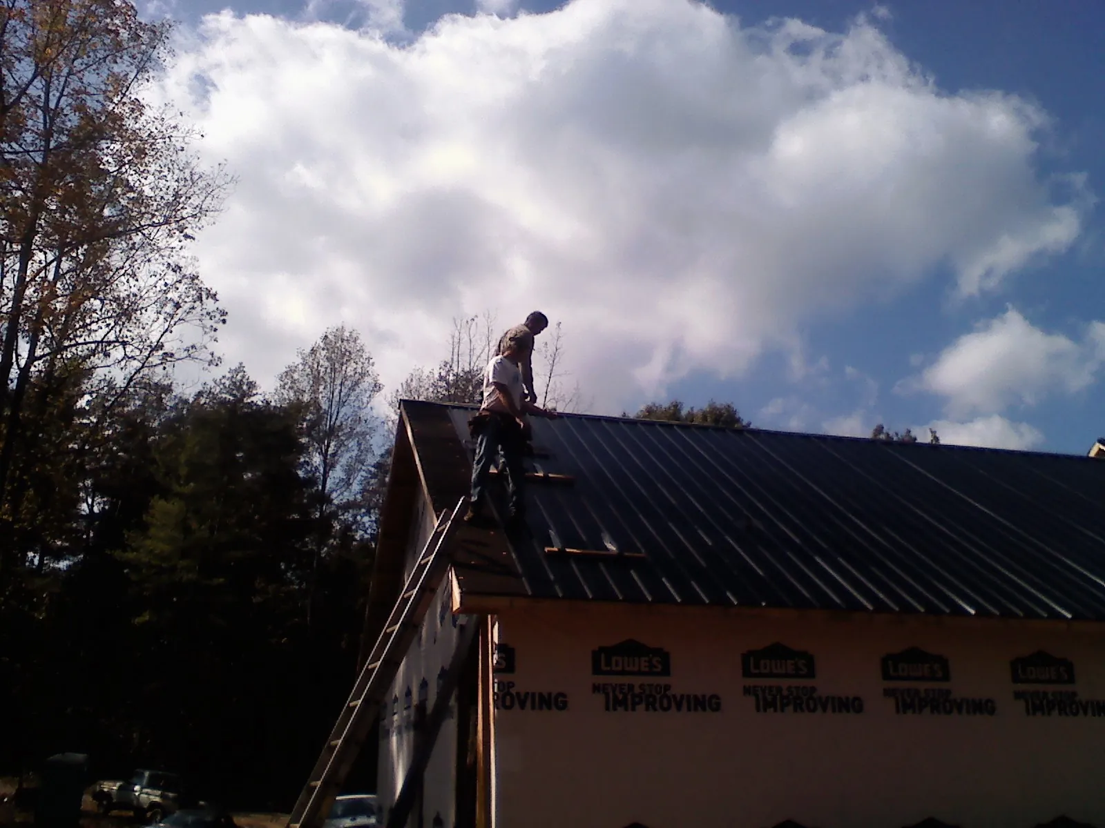 Roofer fastening dark metal panels high against a cloudy sky, from a Roof Inspection job in Vacherie