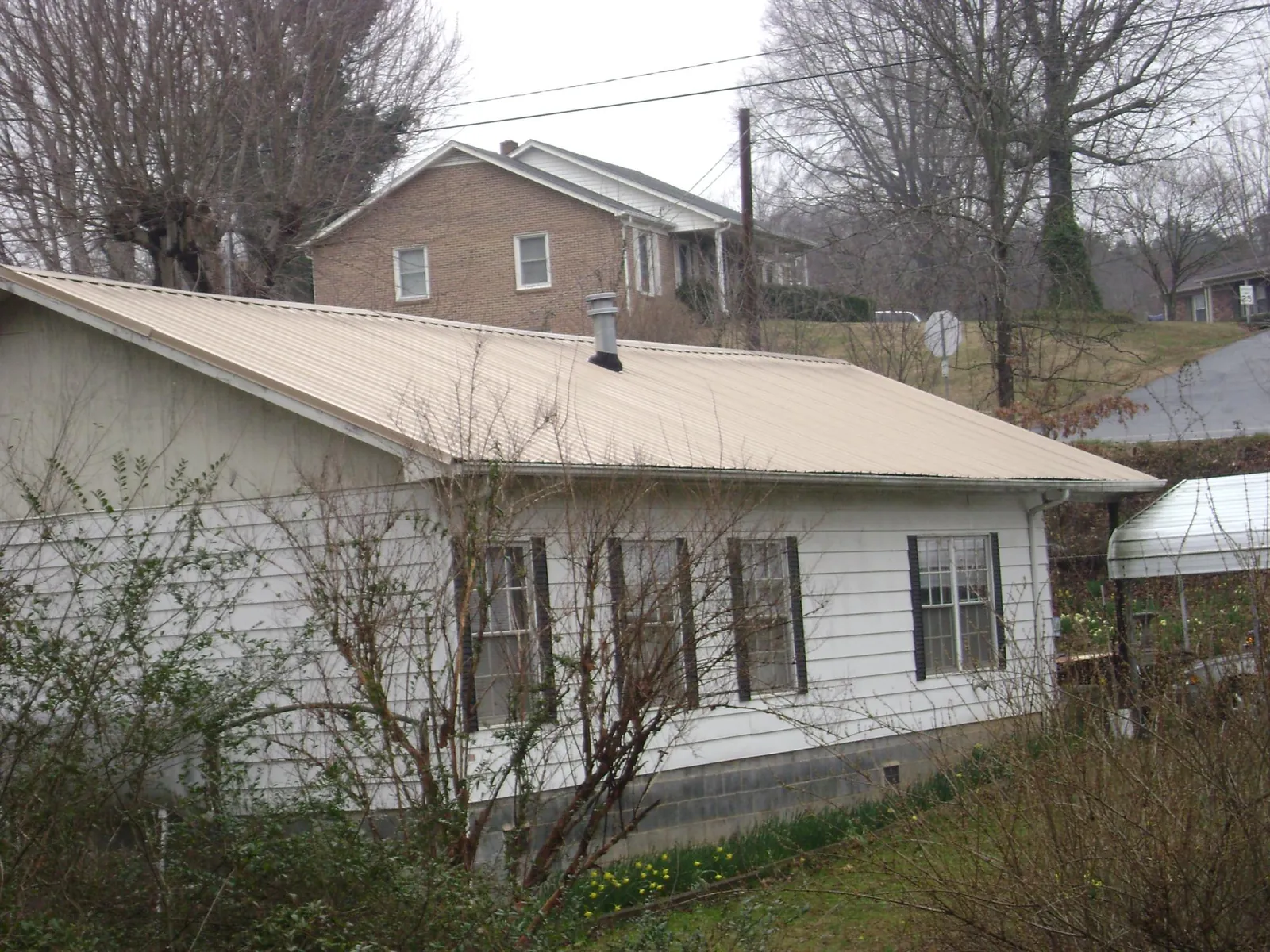 Tan metal roof on a white sided house set into a hillside — Commercial Roofing by Roofing Brothers in Vacherie
